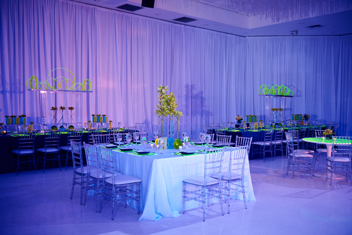 Beautiful guest square table set up for a wedding or social event in the ballroom orchid and lucite chairs draped walls